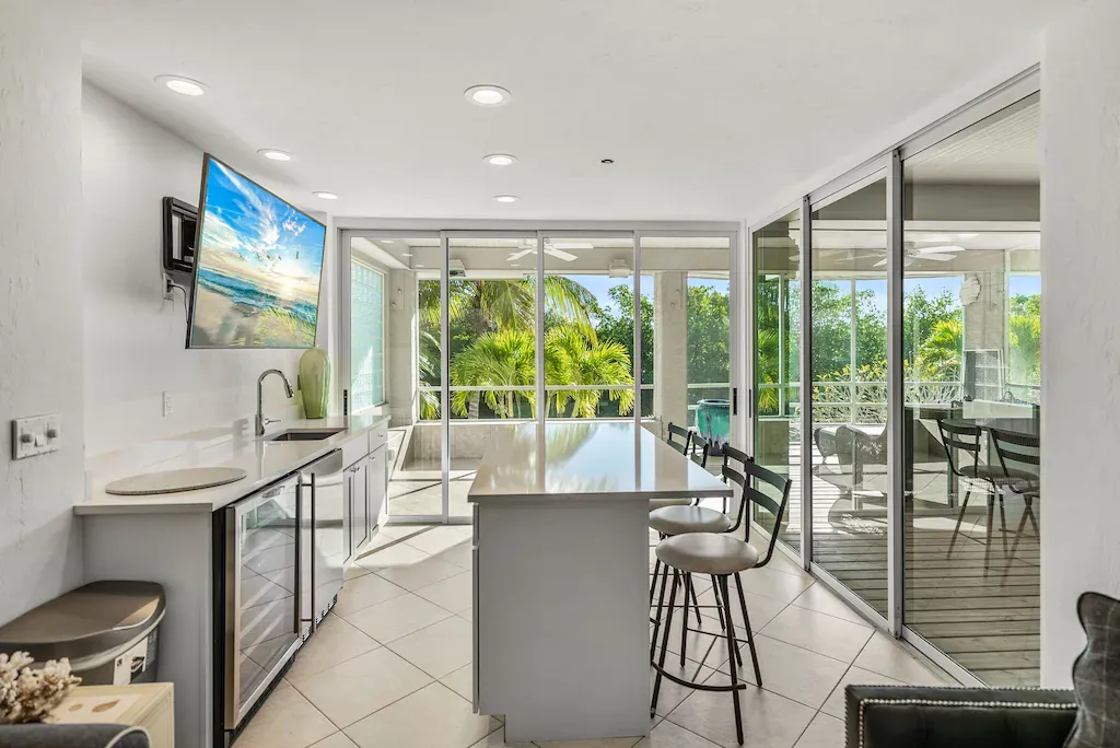 Modern kitchen with a large island, glass doors to a balcony, and a TV mounted on the wall.