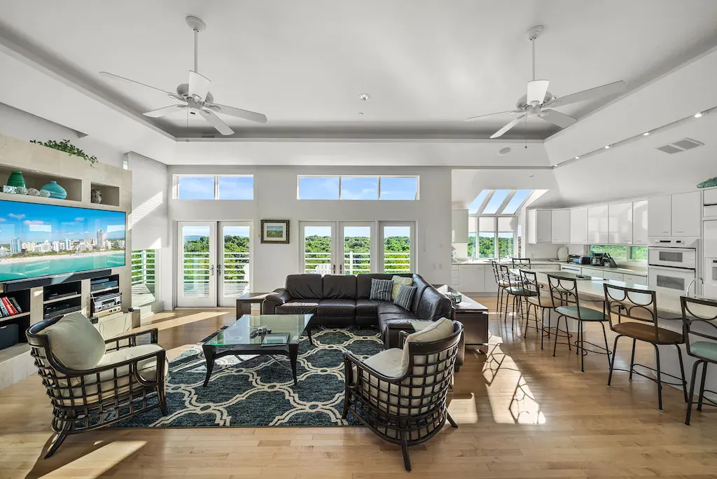 Spacious, modern living room with a sectional sofa, chairs, kitchen, and outdoor views.