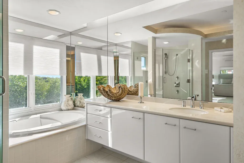 Bright white bathroom with large windows, bathtub, double vanity, and walk-in shower.