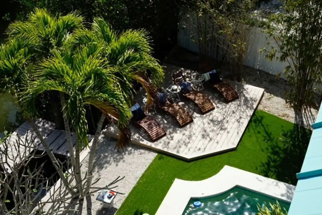 Overhead view of a sun deck with lounge chairs, a pool, and palm trees.