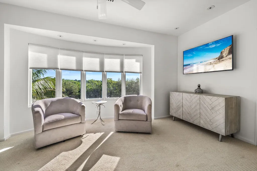 Bright living room with curved window, two armchairs, TV, and console table.