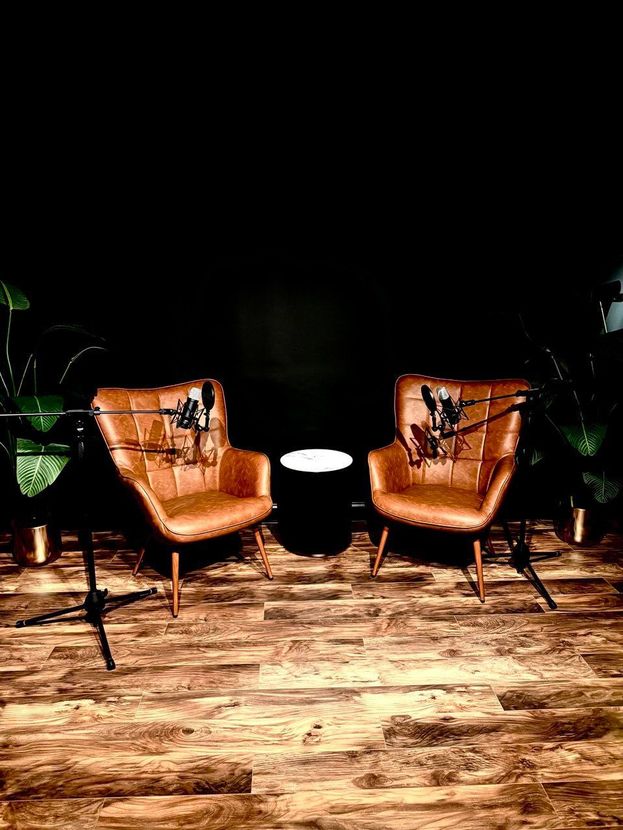 Two brown leather chairs with microphones on them are sitting next to each other on a wooden floor.