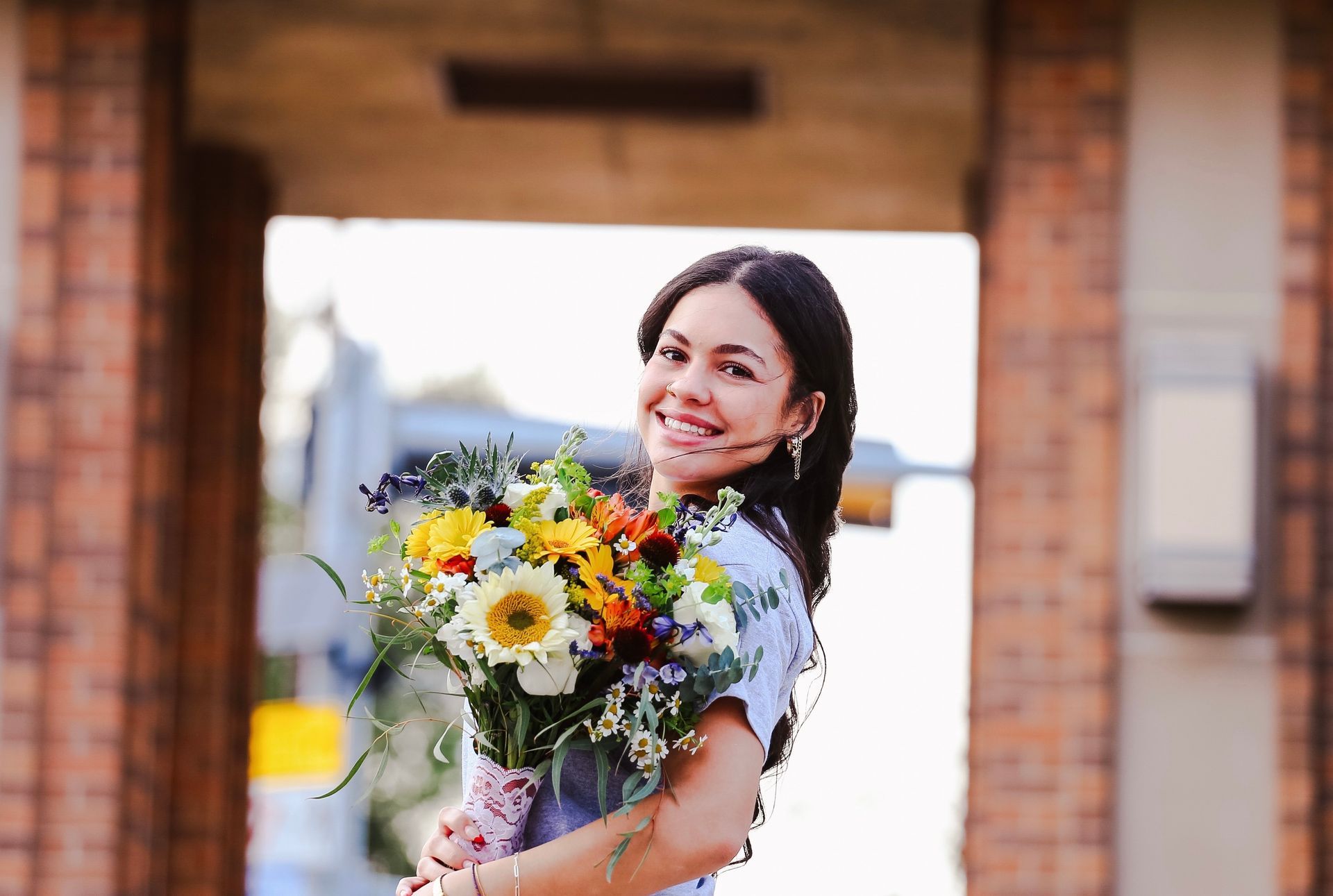 A woman is holding a bouquet of flowers in front of a brick building.