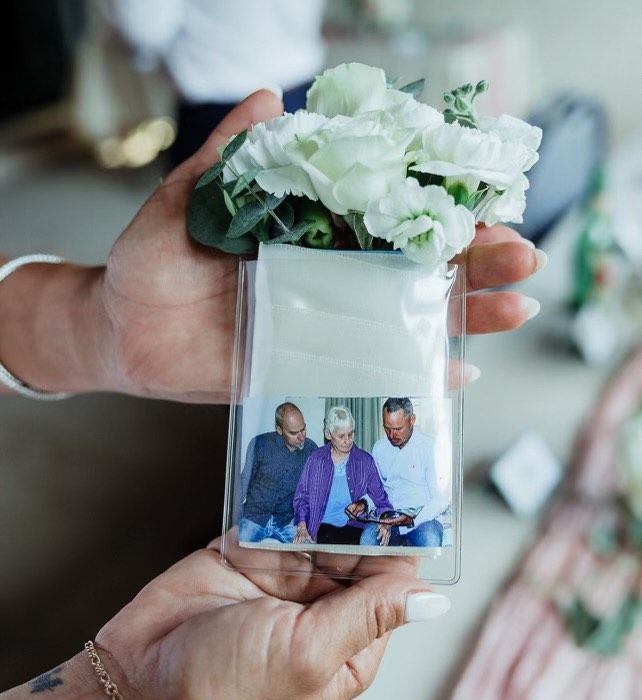 A woman is holding a vase of flowers and a picture of three people