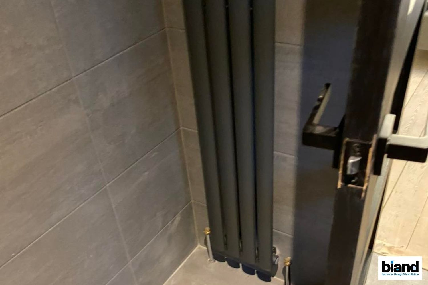 Gray radiator against tiled wall next to a black door.