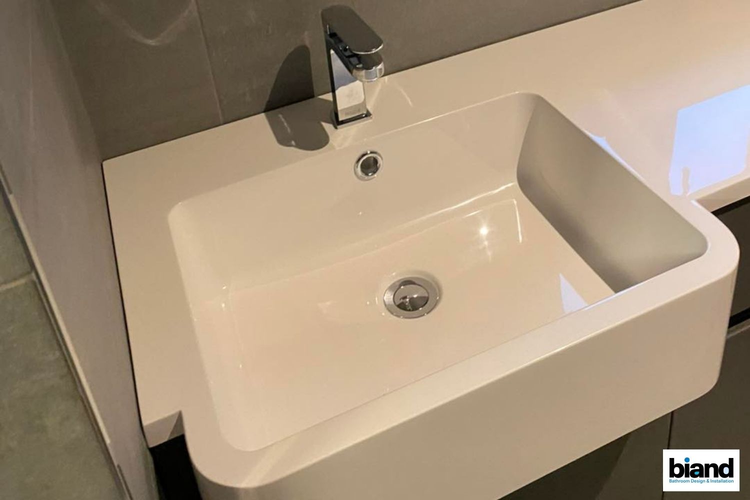 White rectangular bathroom sink with chrome faucet, set in a white countertop with a gray wall backdrop.