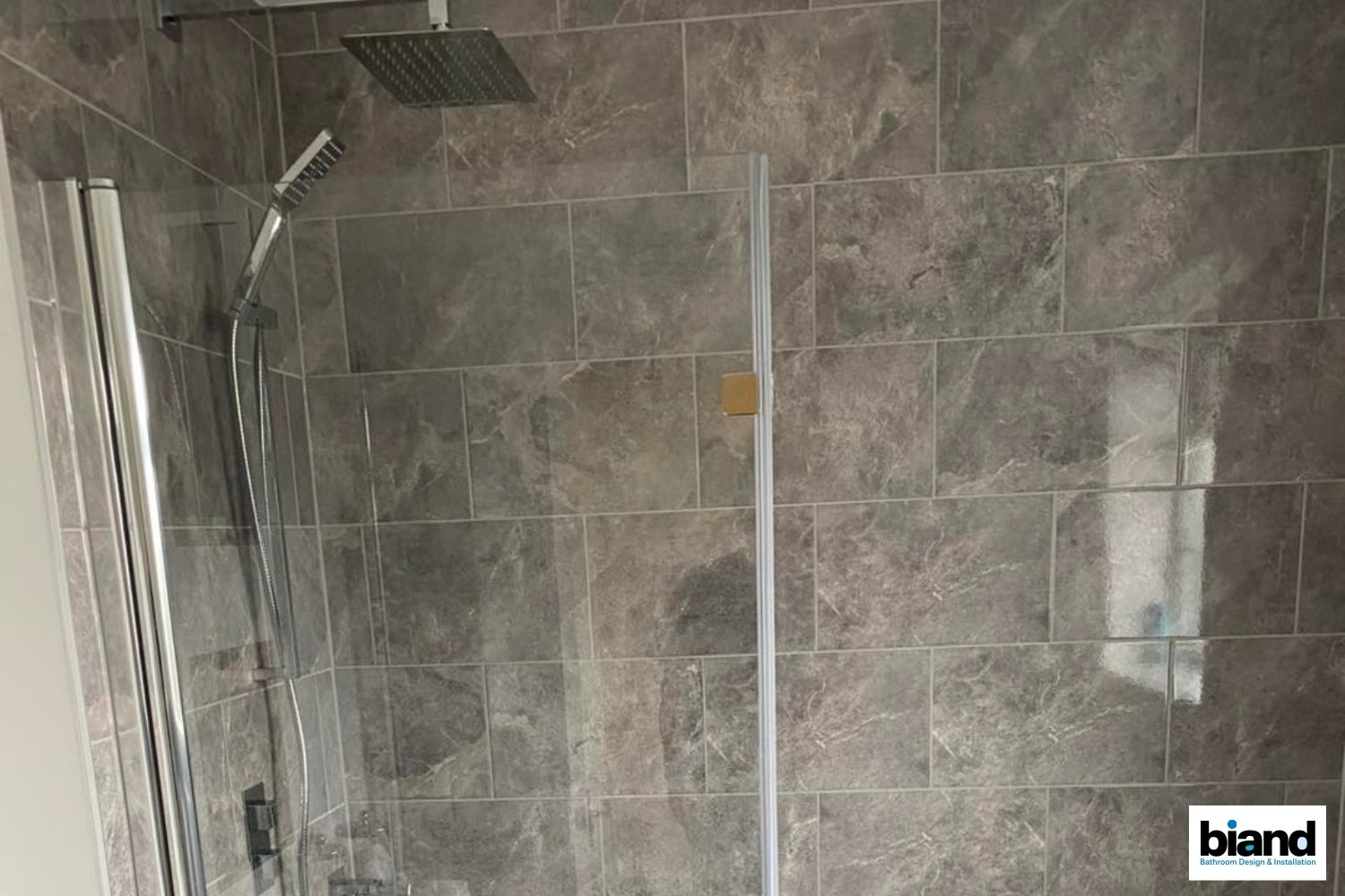 Shower with gray marbled tile, a glass door, and a silver showerhead.