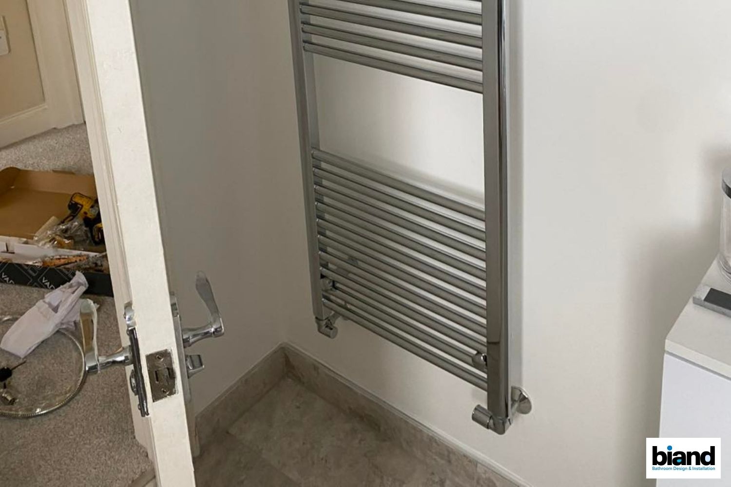 Chrome towel warmer on a white wall in a bathroom.