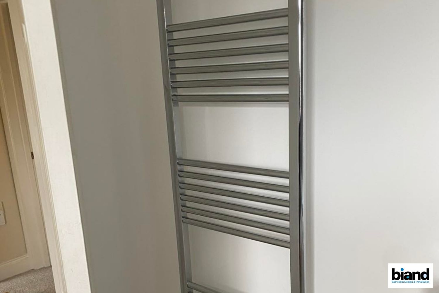 Chrome towel warmer mounted on a light gray wall.