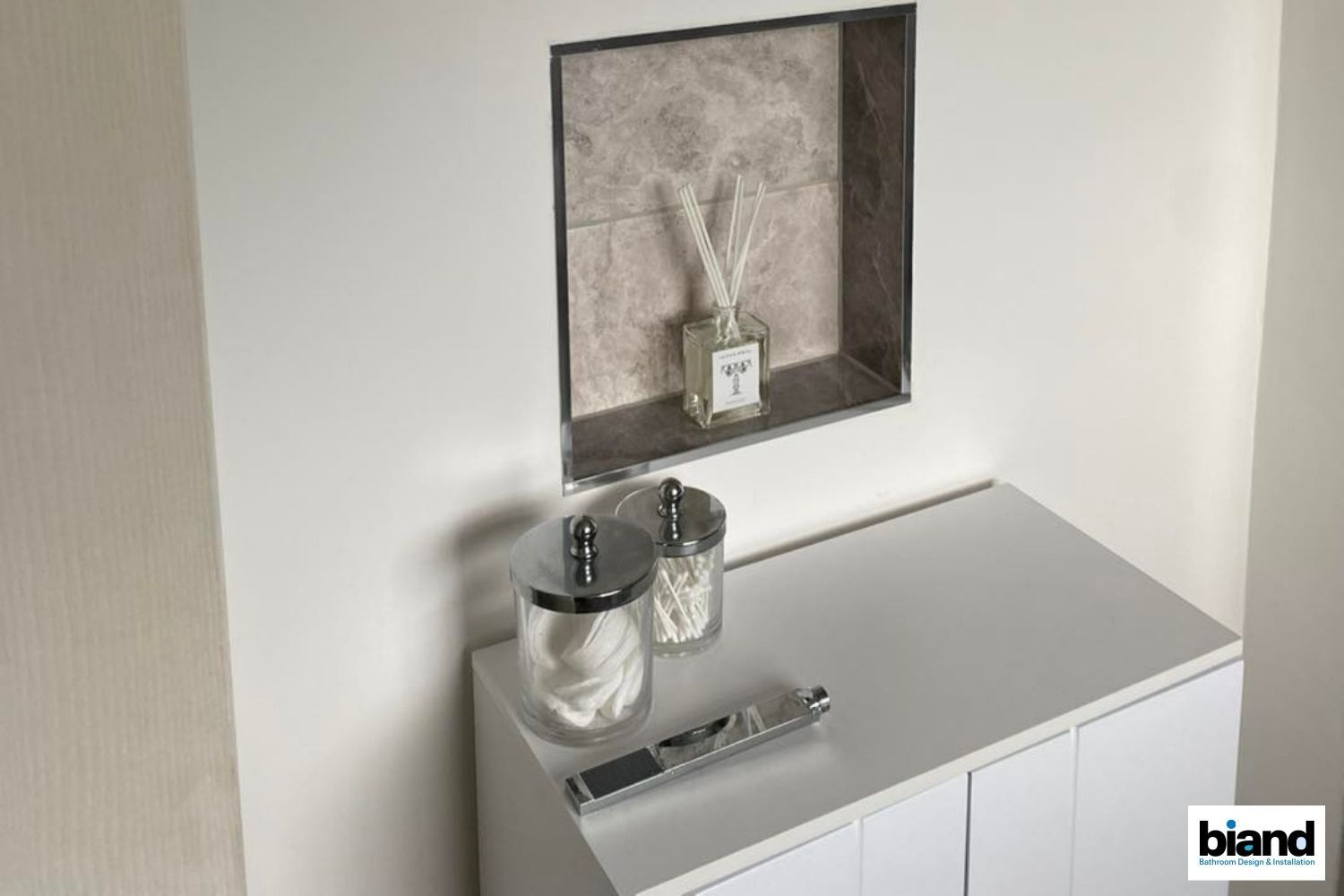 White vanity with toiletries, recessed shelf holding diffuser, neutral tones.