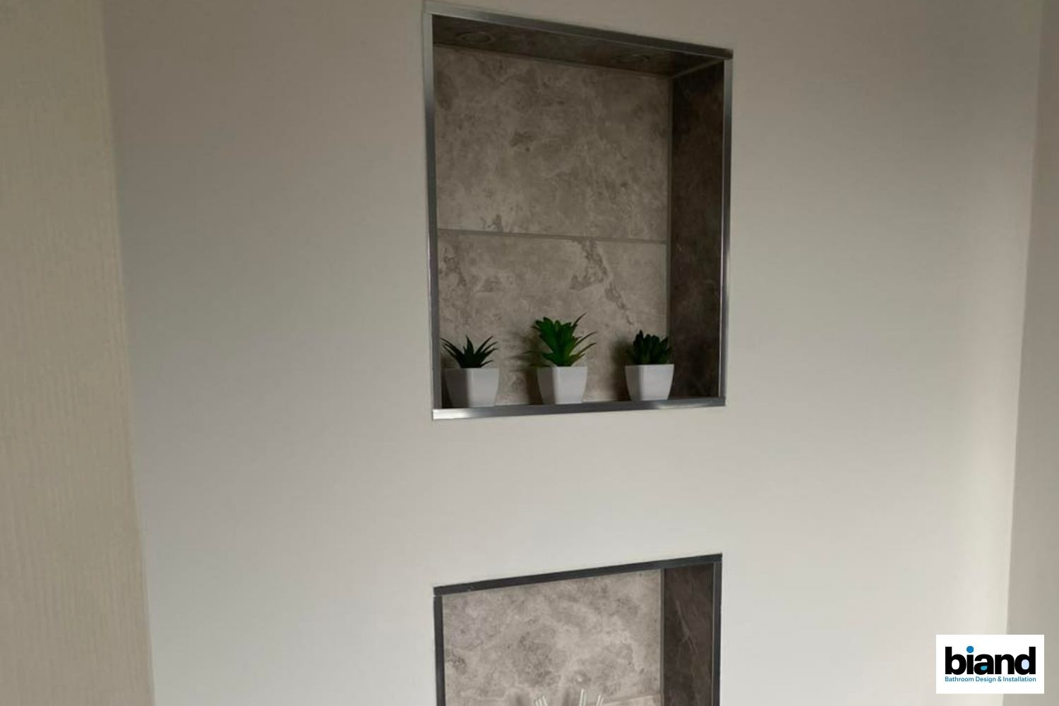 Two recessed wall niches with faux plants, tiled backdrops, and stainless steel trim.