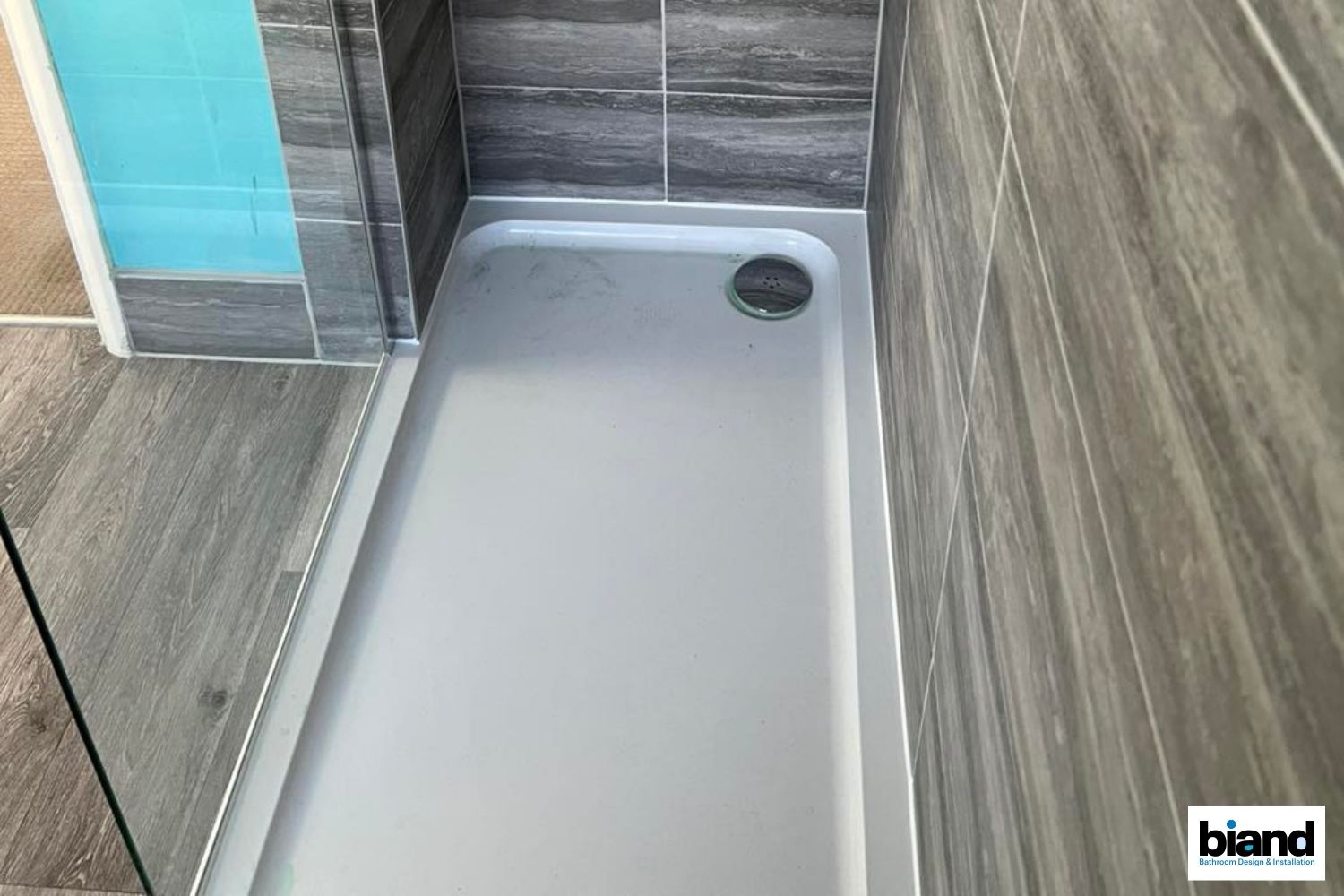 Shower stall with a gray base, gray and wood-look tiled walls, and a blue panel.