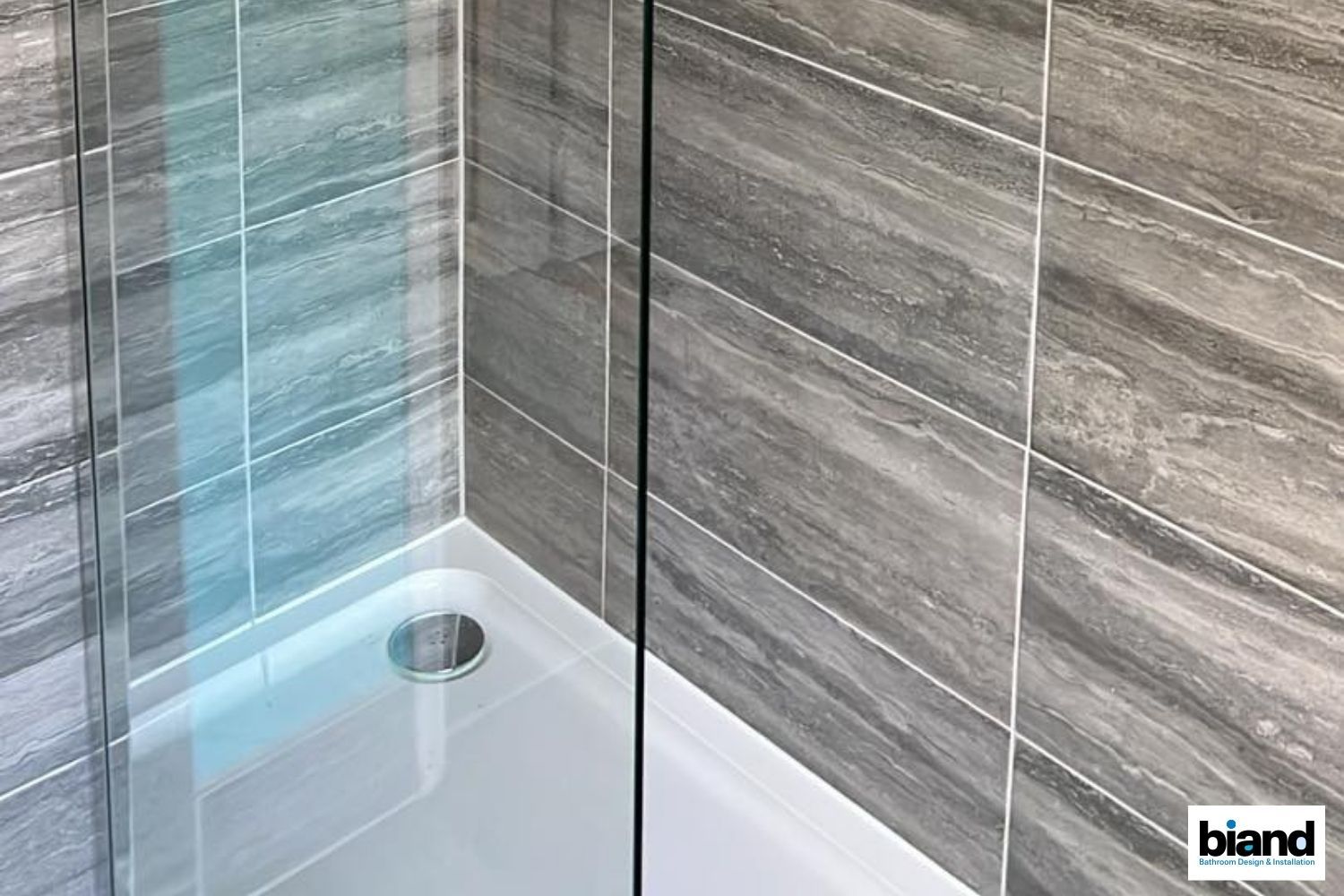 Shower stall with gray tiled walls and a white shower base.