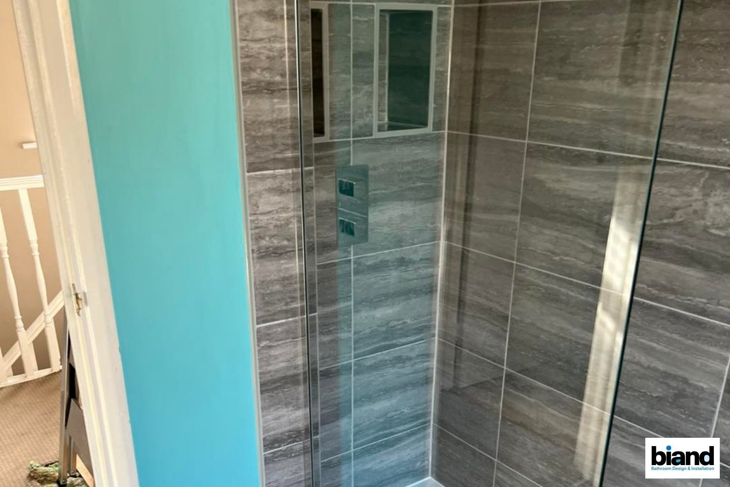 A glass-walled shower with gray tile, blue wall, and silver fixtures.