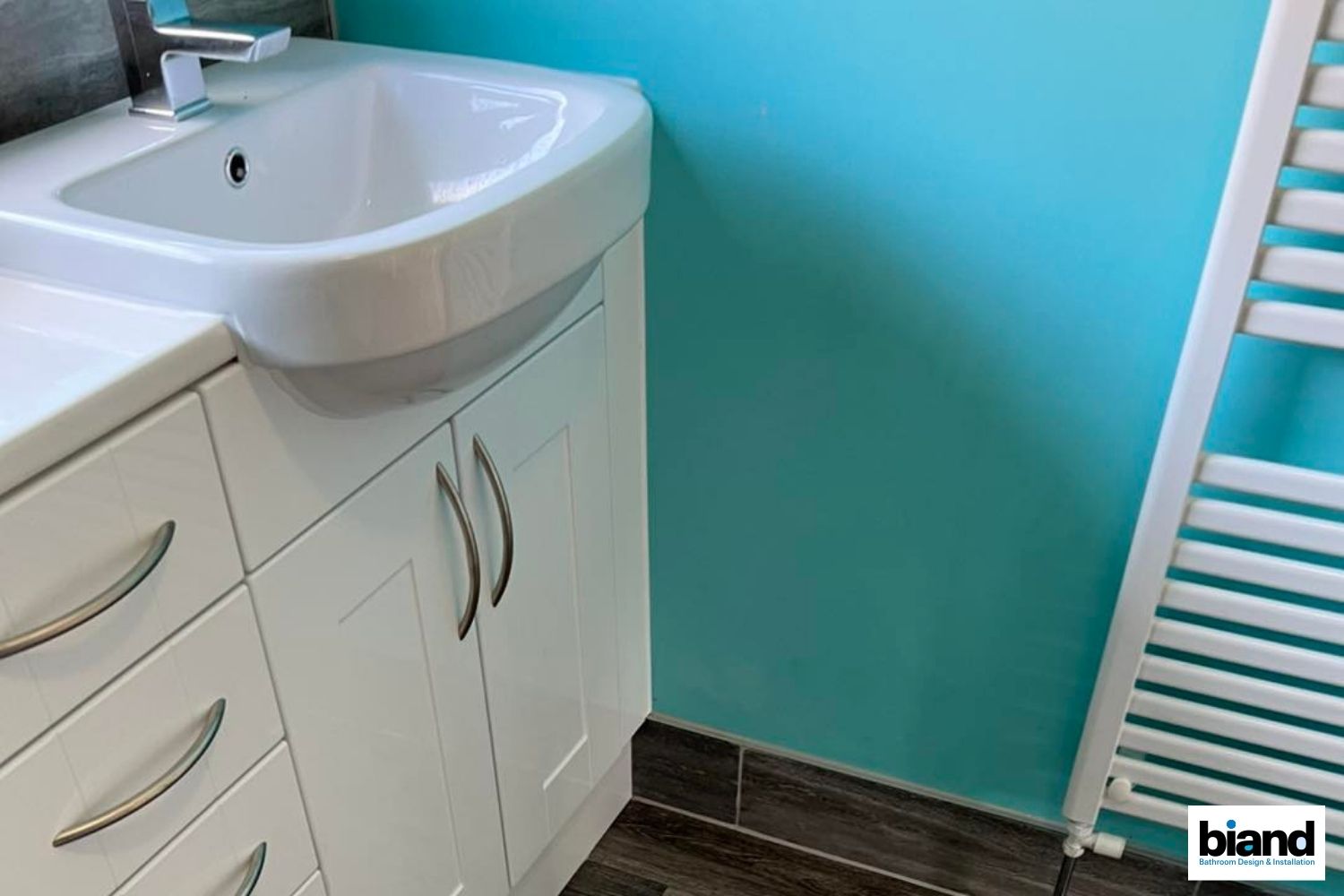 White bathroom vanity and sink against a teal wall, with a radiator on the right.