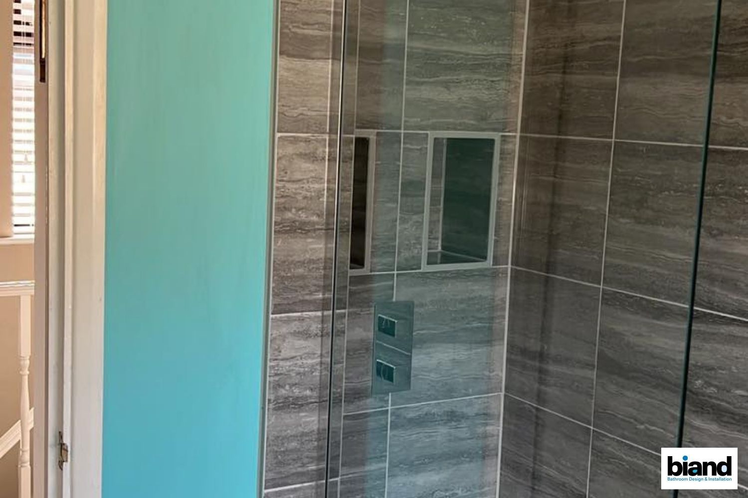 Modern bathroom shower with grey tiled walls, a teal accent wall, and glass door.