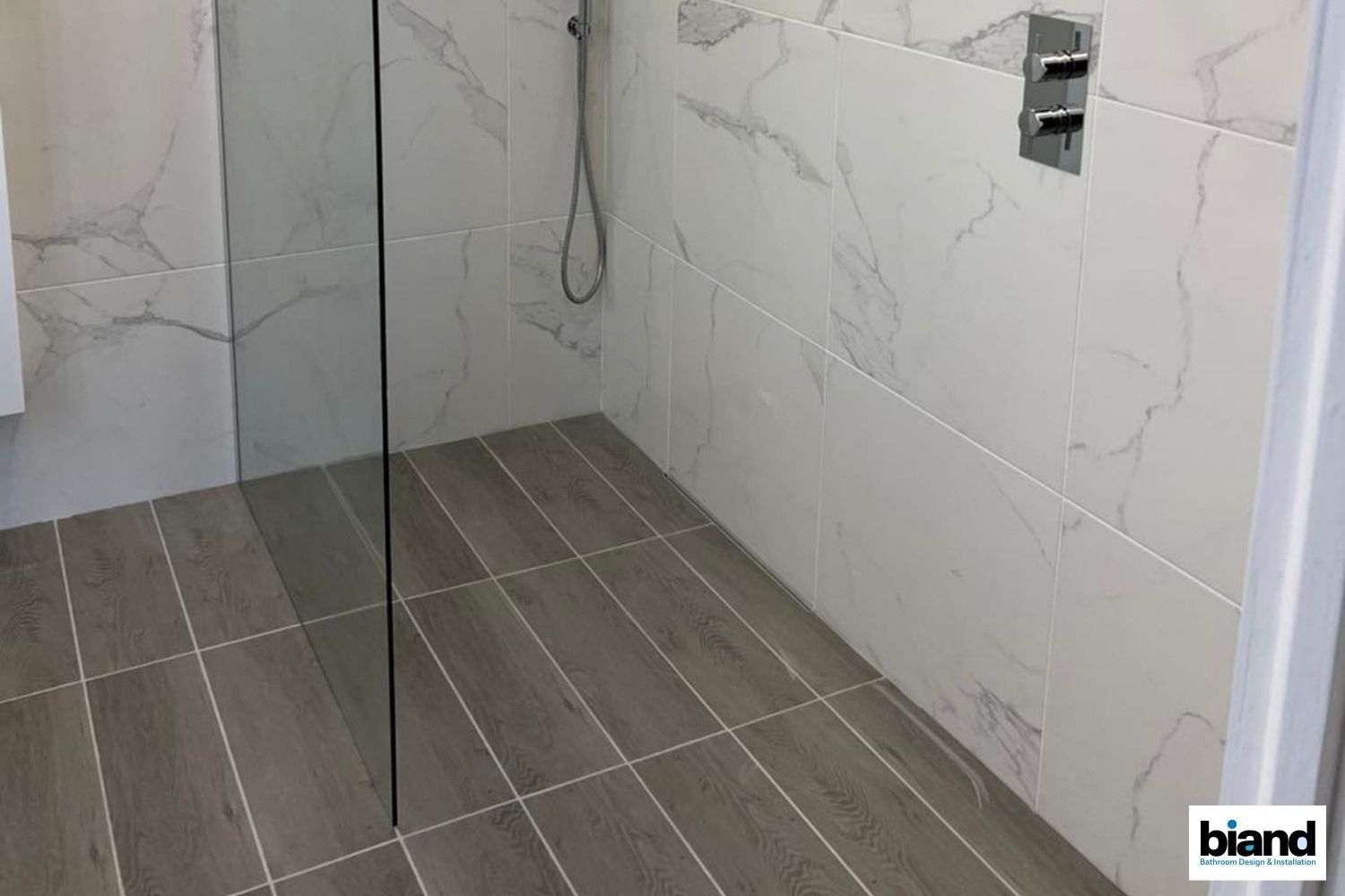 Modern shower with glass door, white marble-look tile on walls, and wood-look tile floor.