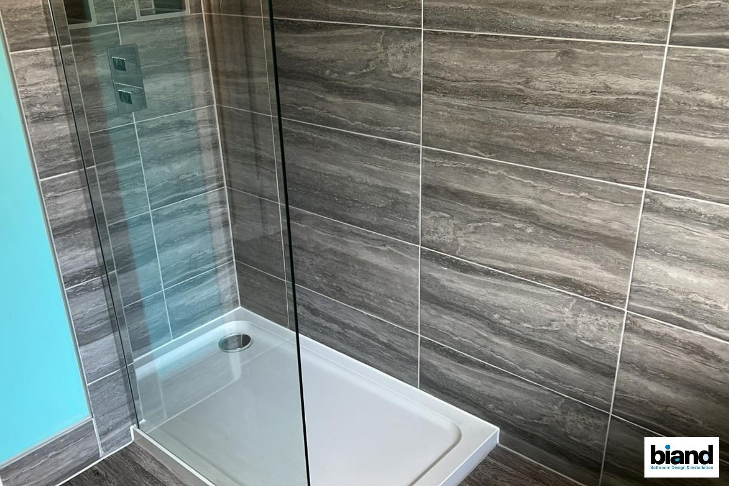 Shower with gray tile walls, glass door, and white shower base; aqua-colored wall visible.