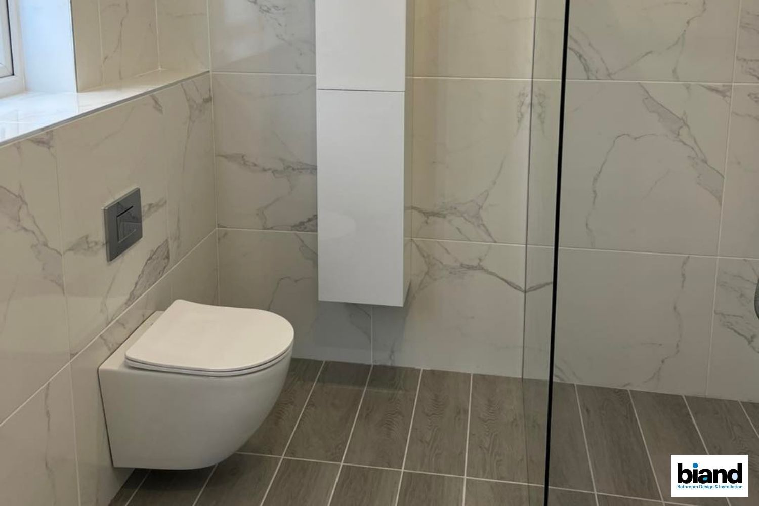 Modern bathroom with a wall-hung toilet, marble-patterned tiles, and a white cabinet.