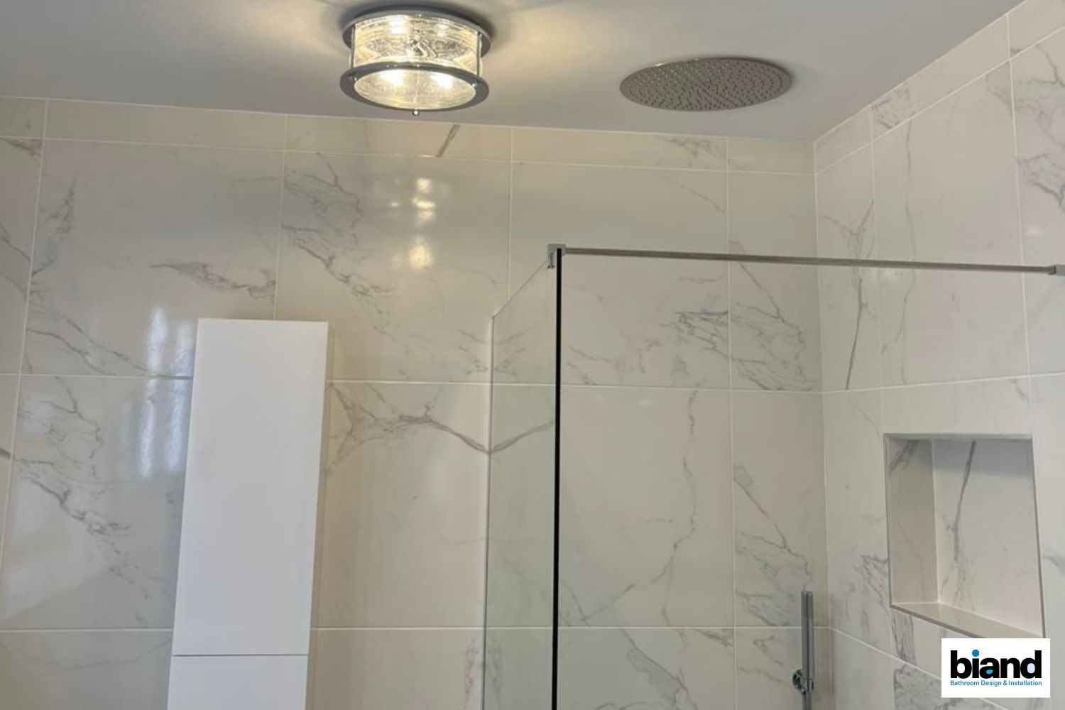 White tiled bathroom with a shower, recessed shelf, glass door, and a flush-mounted light fixture.