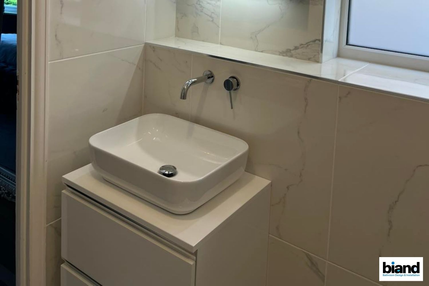 Modern white bathroom with a rectangular sink on a cabinet, wall-mounted faucet, and tiled walls.