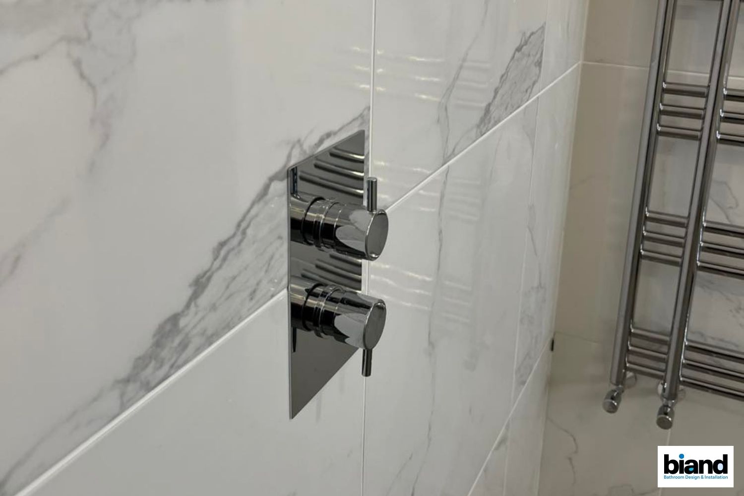 Chrome shower controls on white marble tile, next to a chrome towel rack.