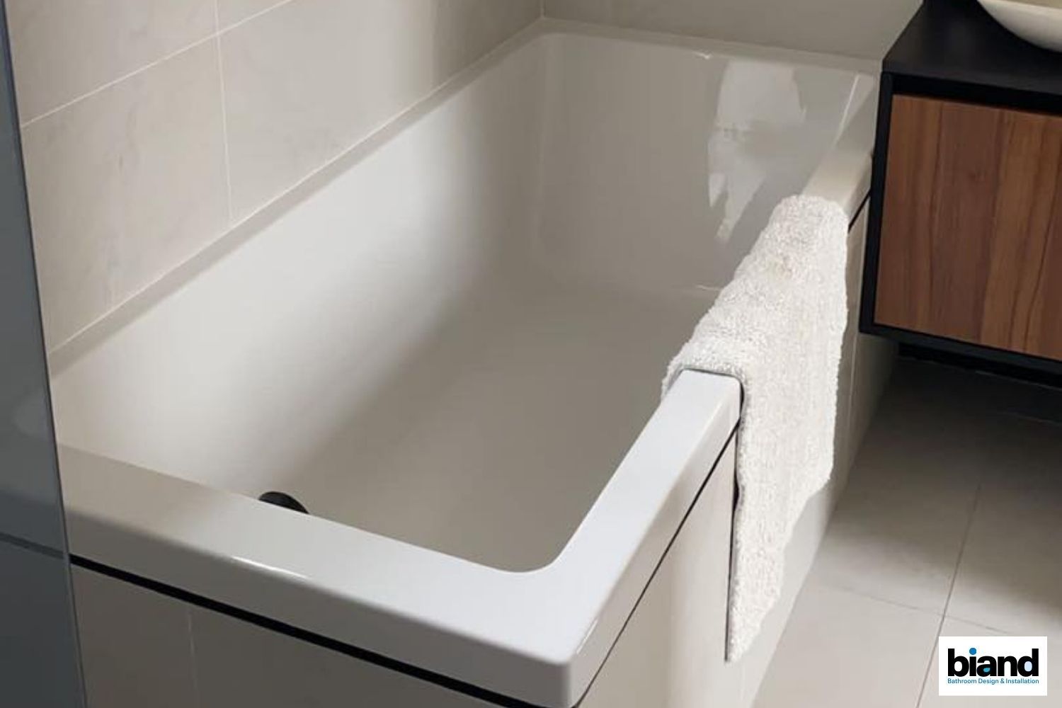 White bathtub in a modern bathroom, with a towel draped over the side.