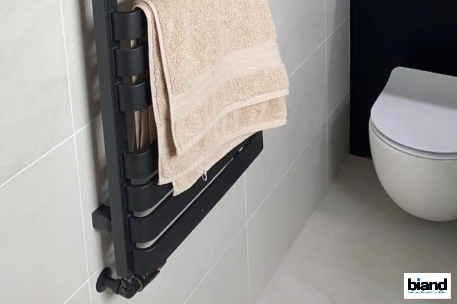 Black towel warmer with a tan towel in a bathroom, next to a toilet.