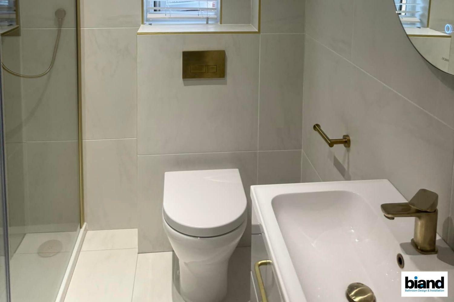 Modern bathroom with white fixtures, gray tiles, and gold accents.