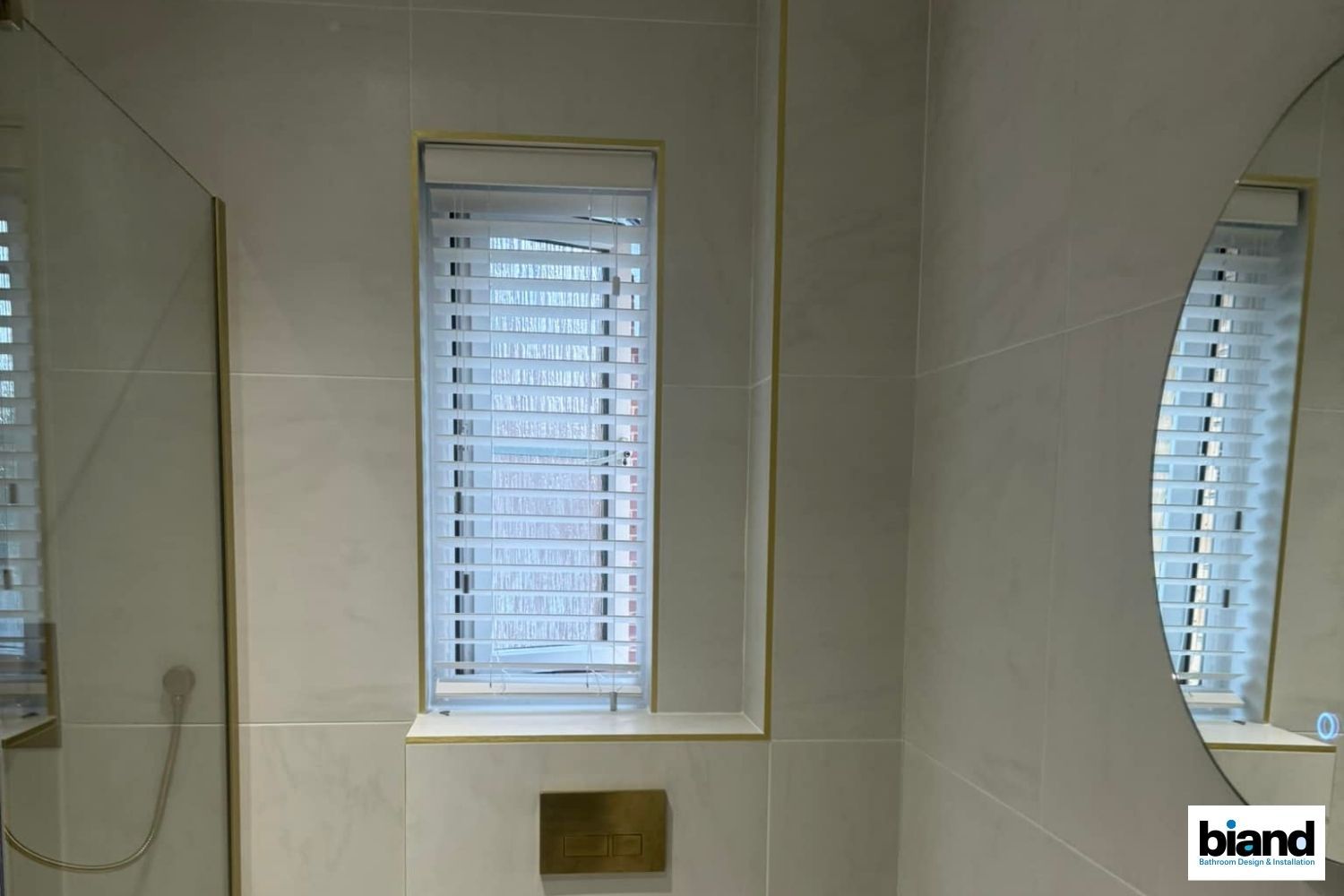 Bathroom with window, blinds, gold trim, and a round mirror.