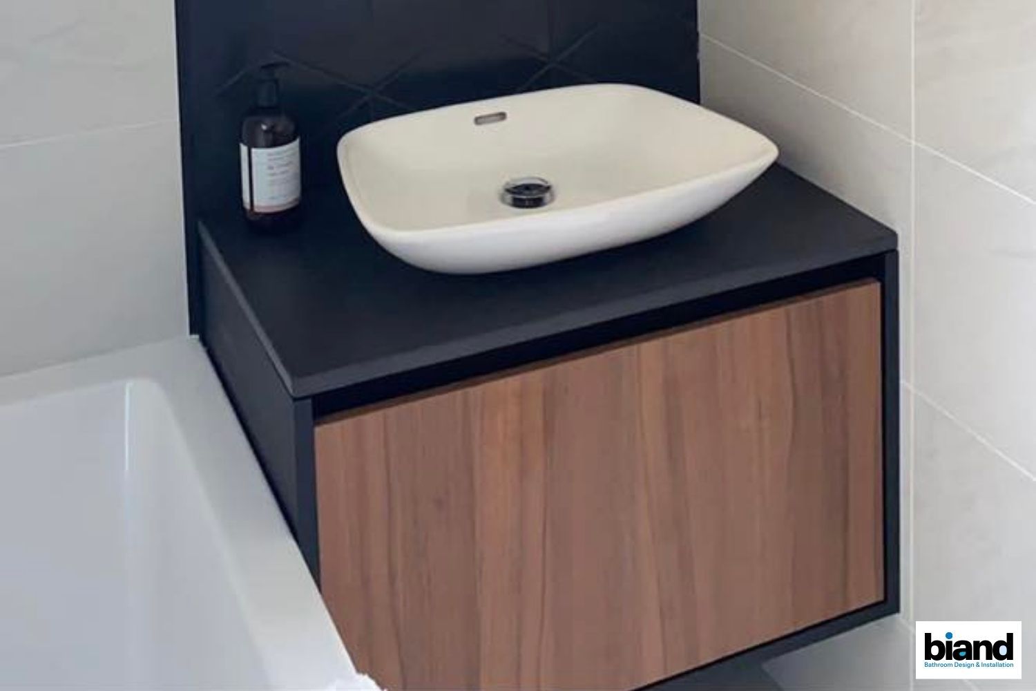 Bathroom vanity with a wood-grain cabinet and black countertop, white oval sink, and a black soap dispenser.