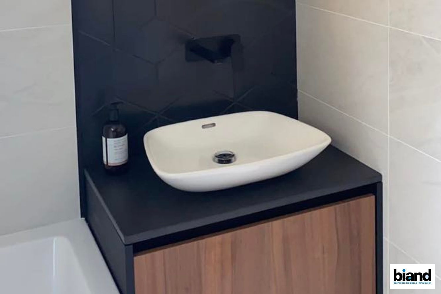 Bathroom vanity with a white vessel sink on a black countertop and wood cabinet.