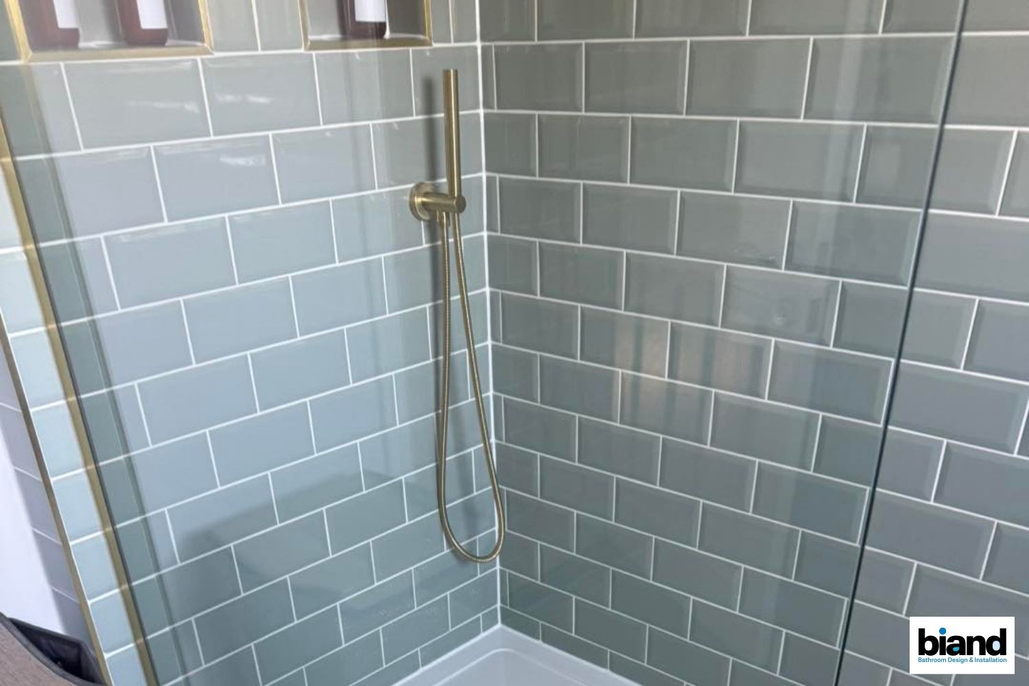 Shower stall with pale blue subway tiles and gold fixtures.