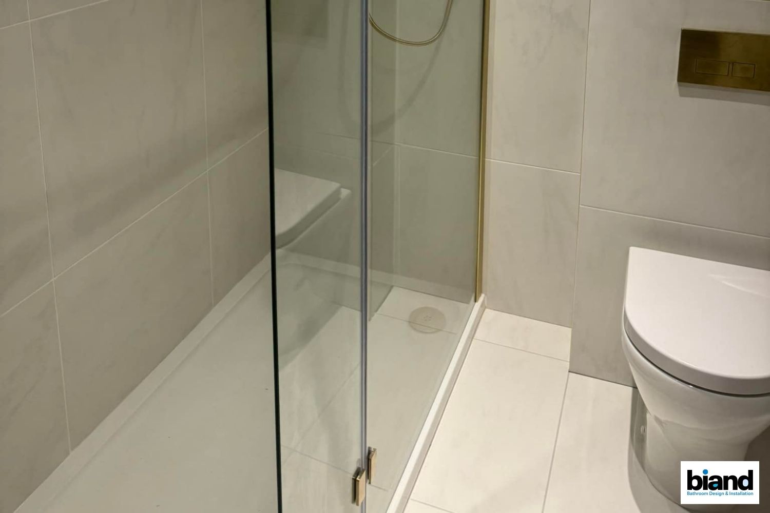 Bathroom with a shower, toilet, and white tiled walls. The shower has a glass door.