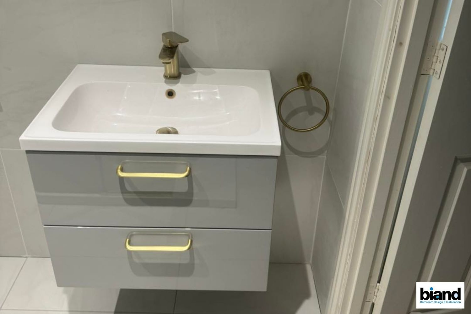 Gray vanity with a white sink, gold faucet and towel ring.