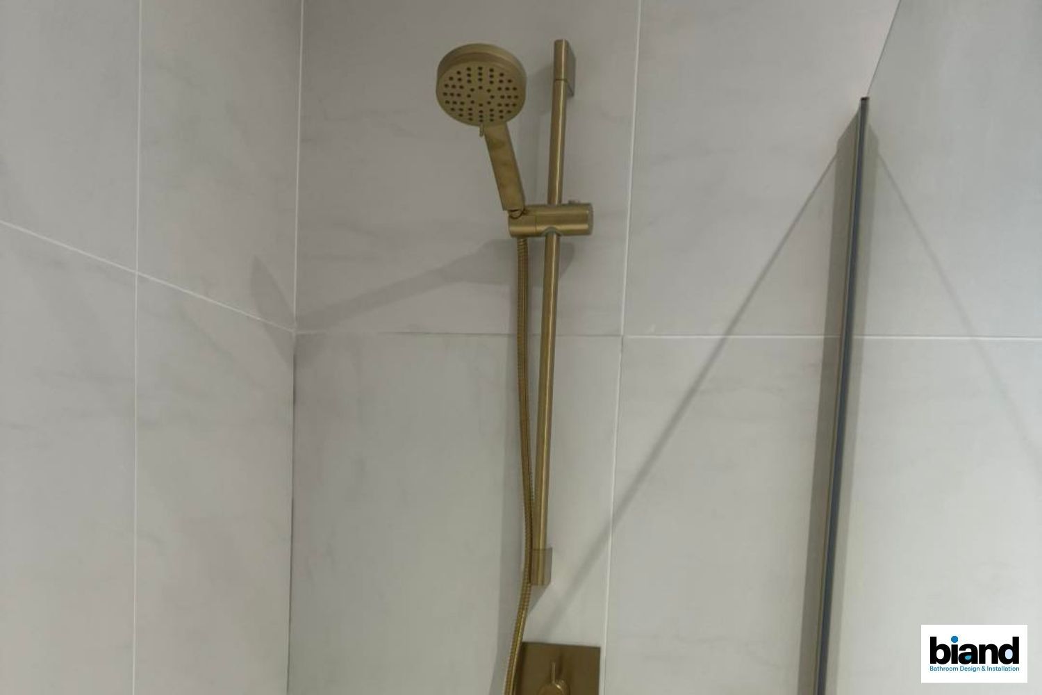 Gold shower head and rail on light gray tiled wall.