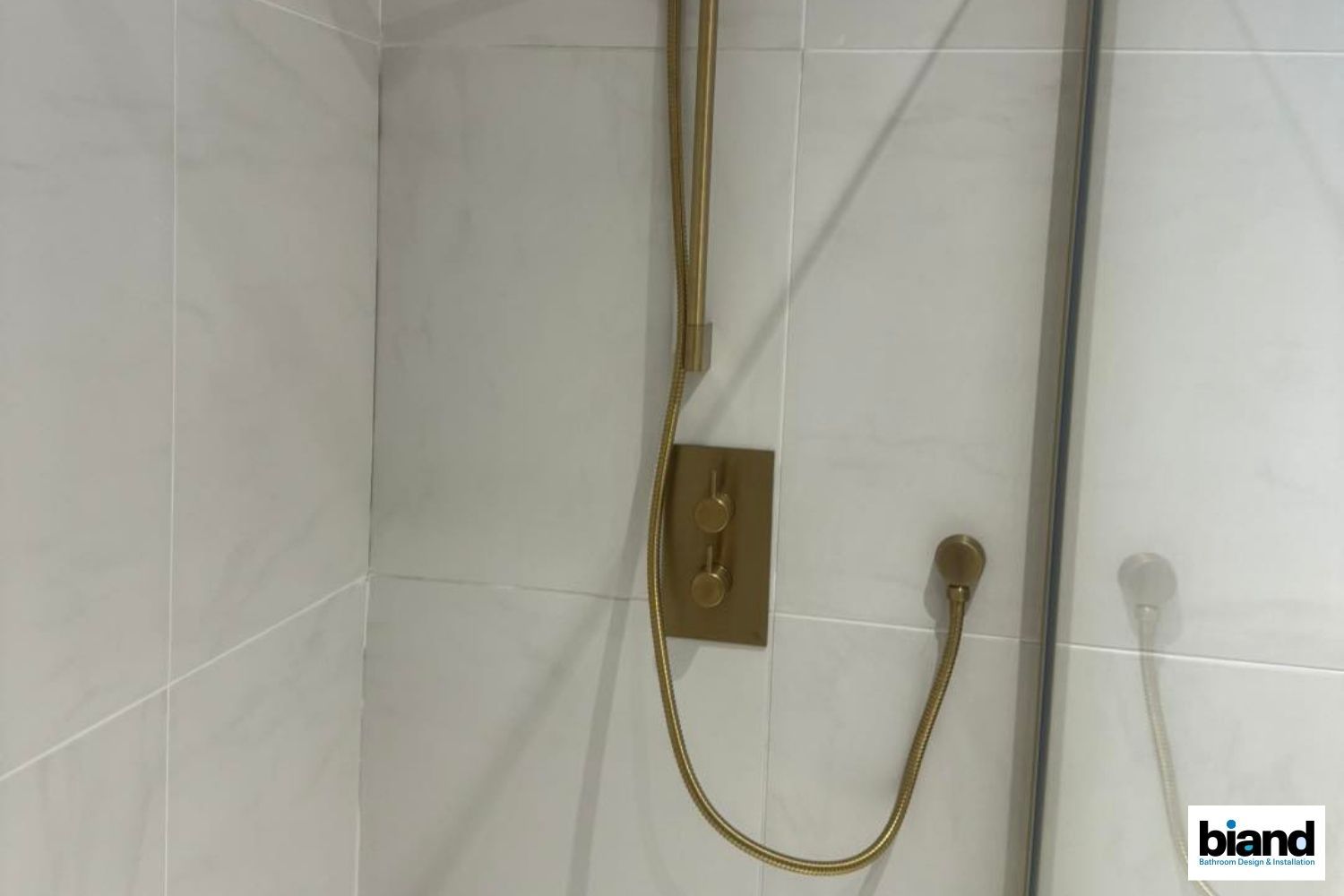 Gold shower fixtures in a white tiled shower stall.