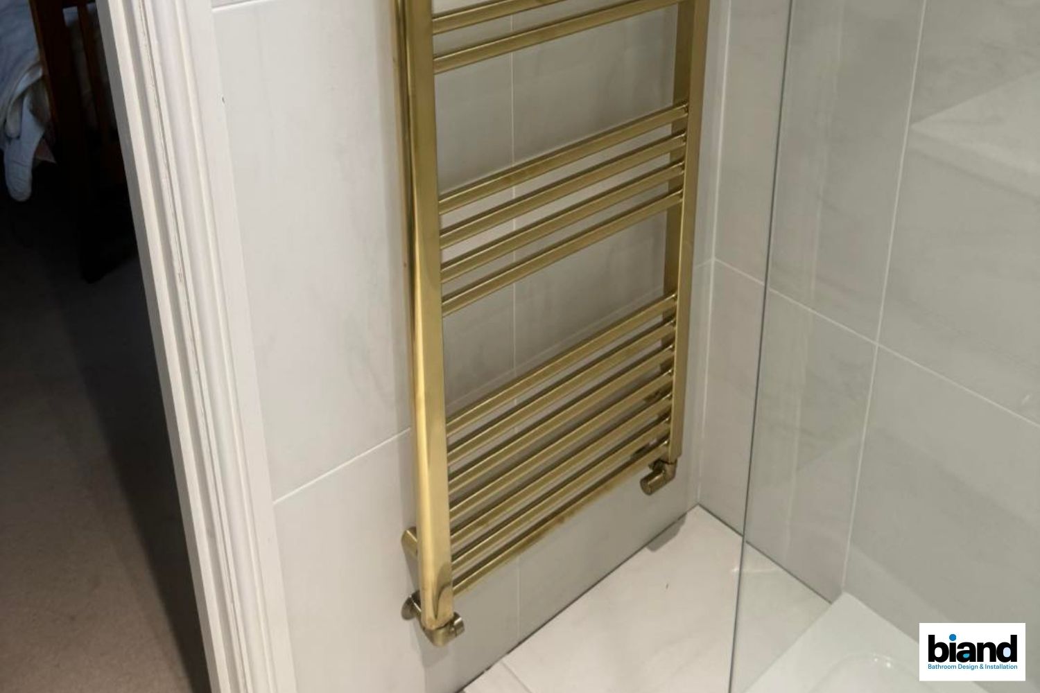 Gold towel warmer on light gray tiled wall in a bathroom.