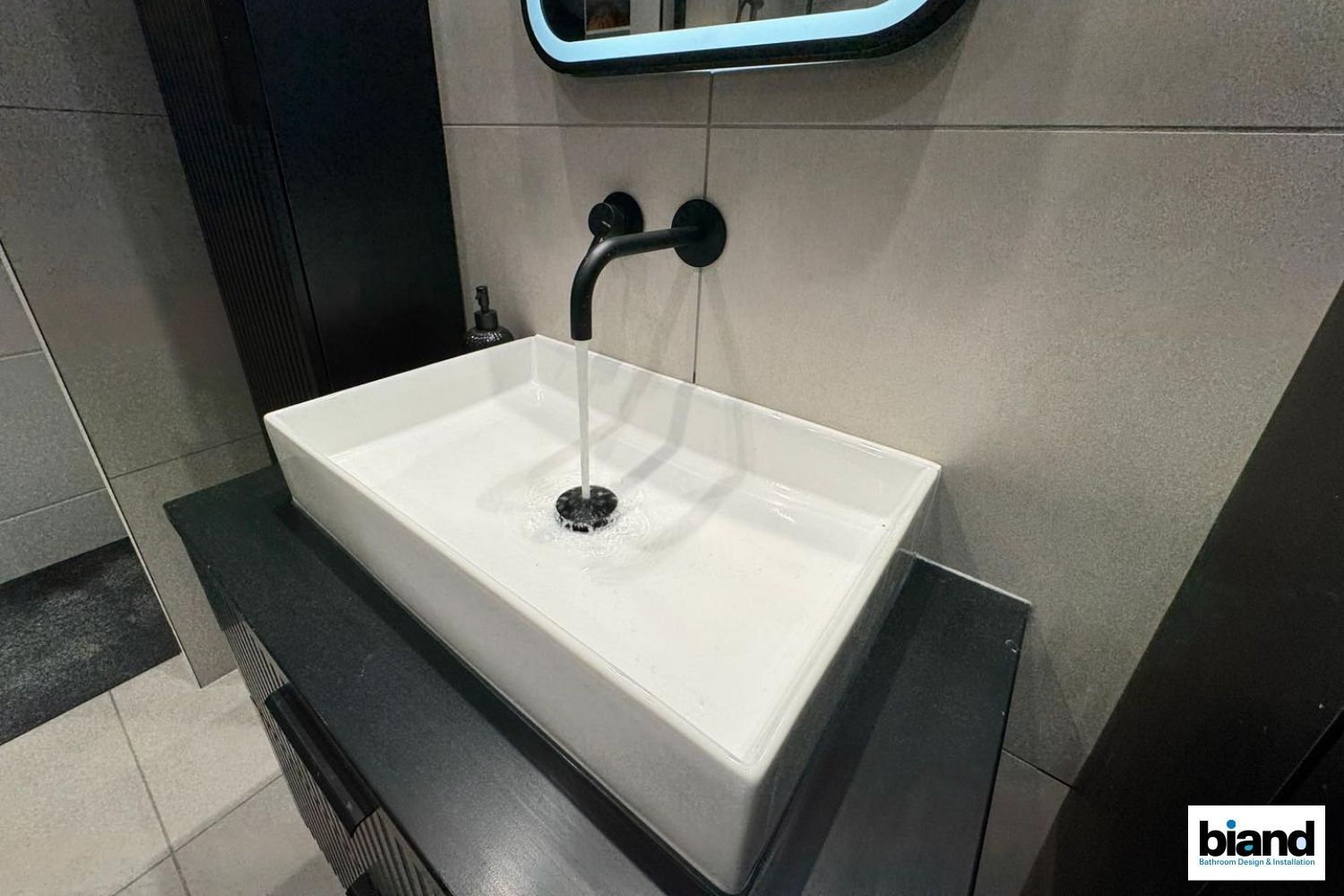 Black faucet pours water into a white rectangular sink in a modern bathroom.