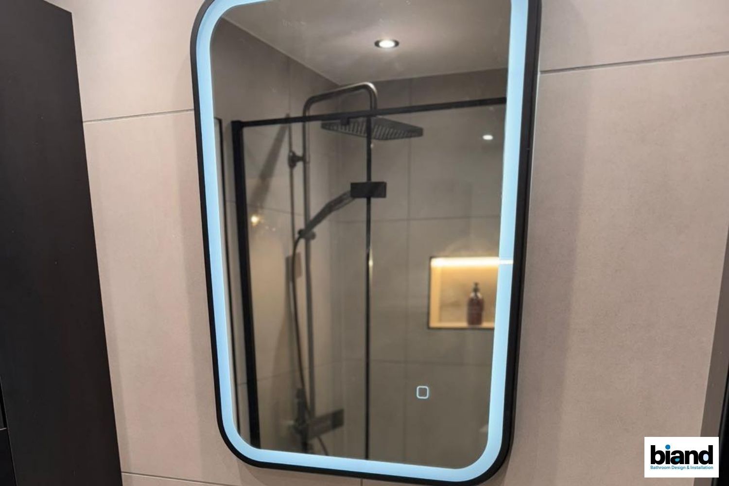 Mirror with a glowing frame reflecting a shower stall and a light-up shelf.
