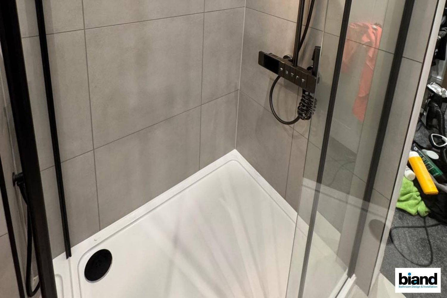 A corner shower with a black frame, gray tile walls, and a white base.