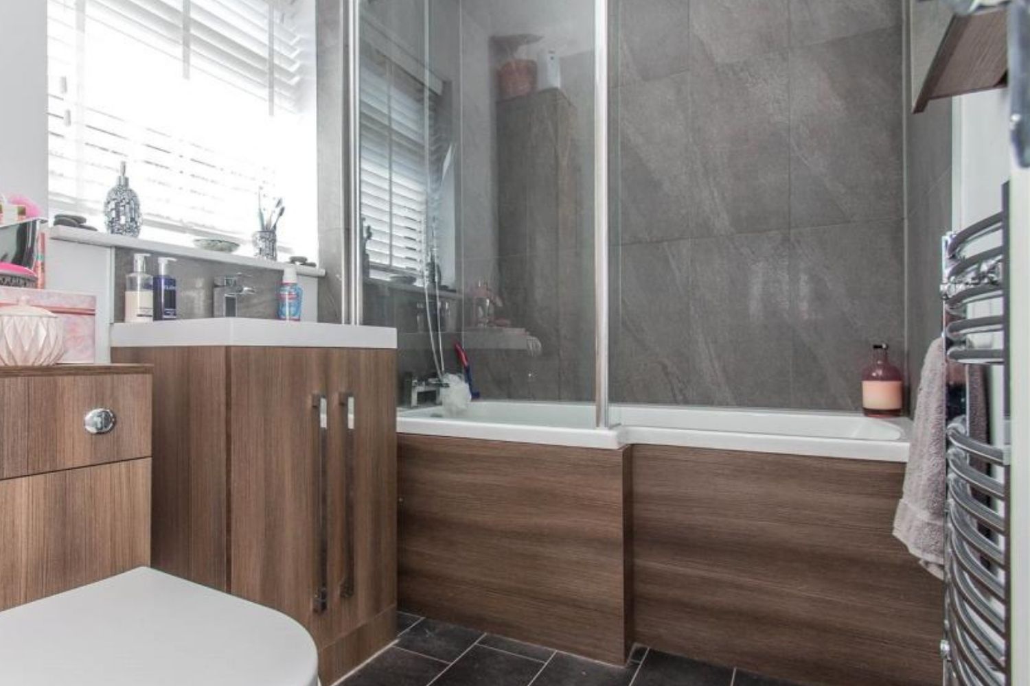 Small modern bathroom with brown cabinets, gray tile, and a shower over a bathtub.