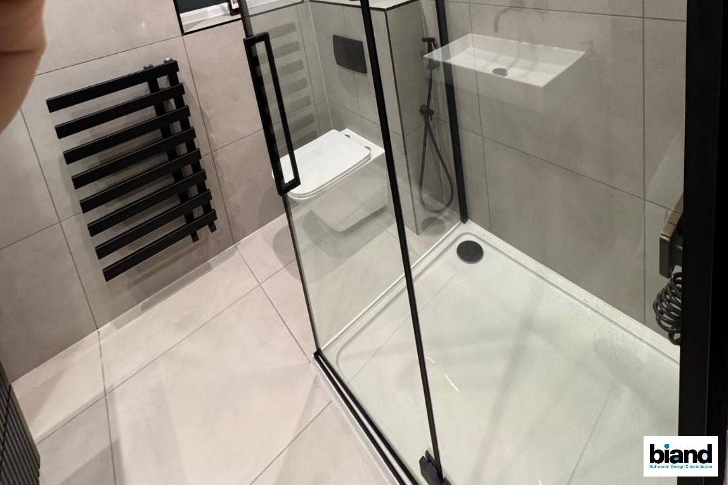 Modern bathroom with black-framed glass shower, toilet, and black towel rack on white tiles.