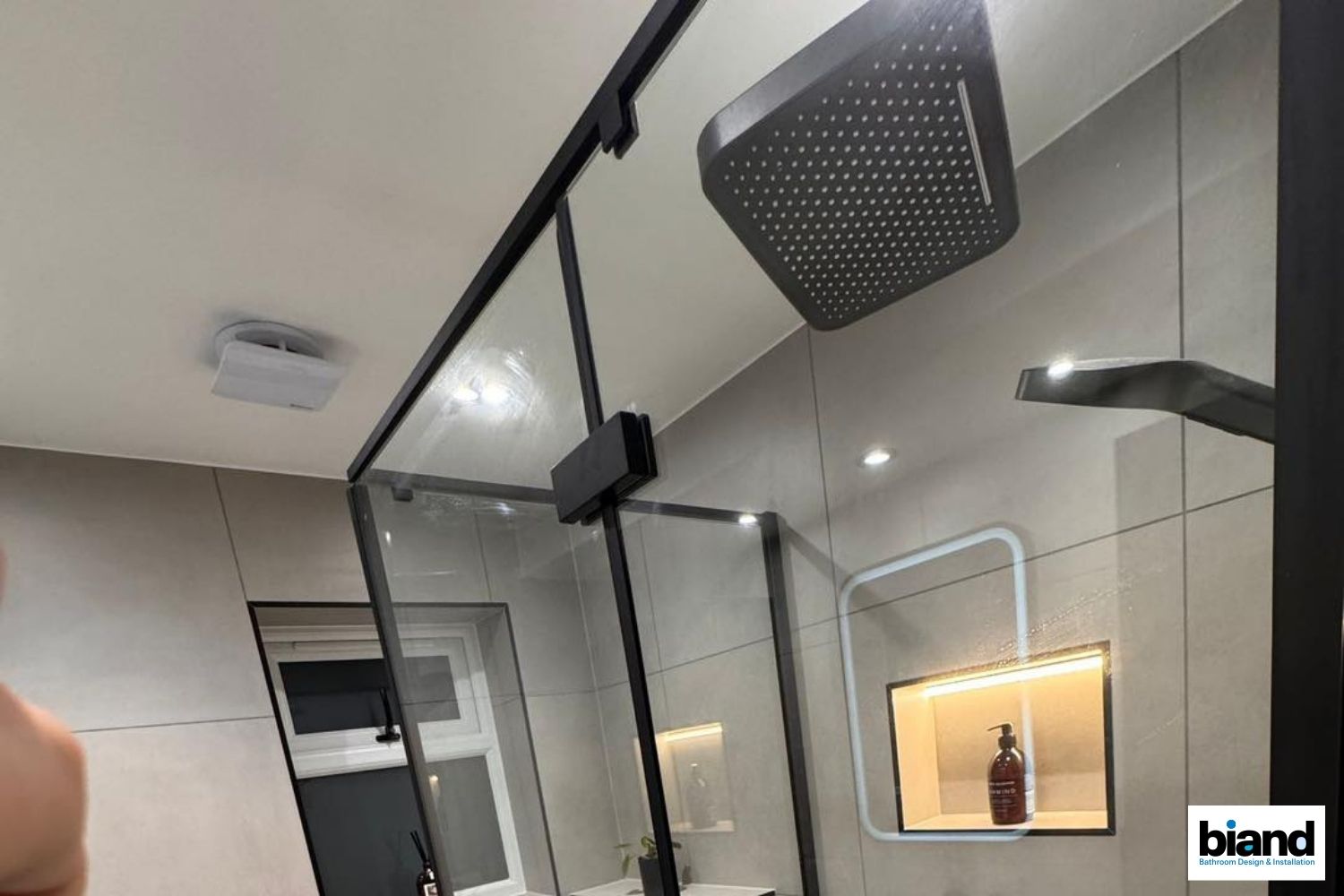 Modern shower with black frame, glass doors, and rain showerhead in a light-colored bathroom.