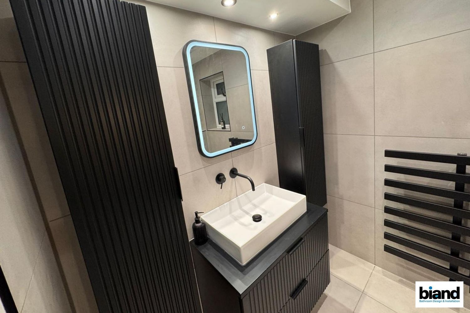 Bathroom with black cabinets, a white sink, a mirror with a blue glow, and a black towel rack.