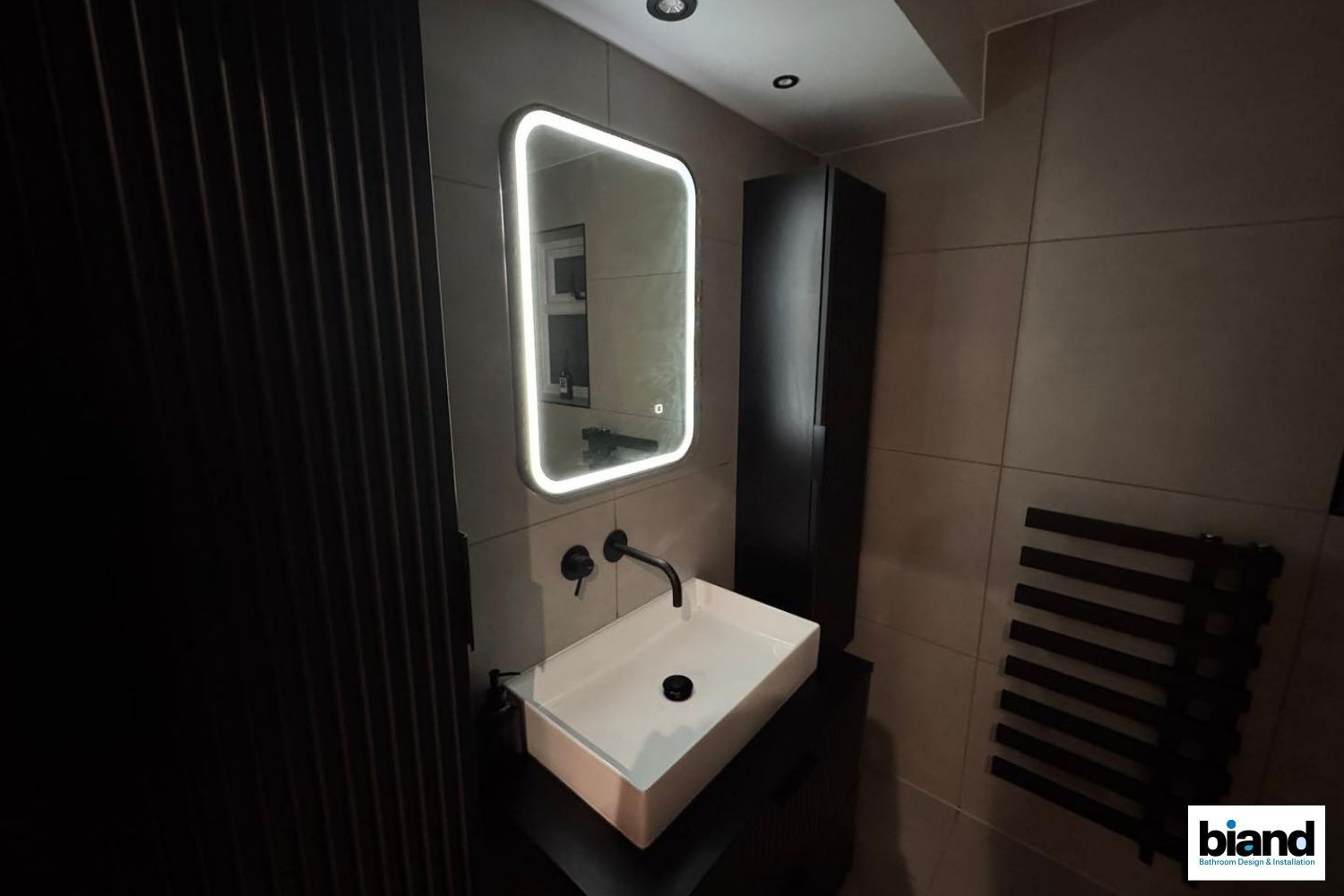 Modern bathroom with a backlit mirror, black fixtures, and a black cabinet.