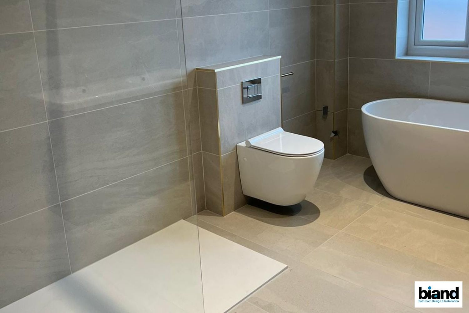 Modern bathroom with light gray tiles, white toilet, and tub.