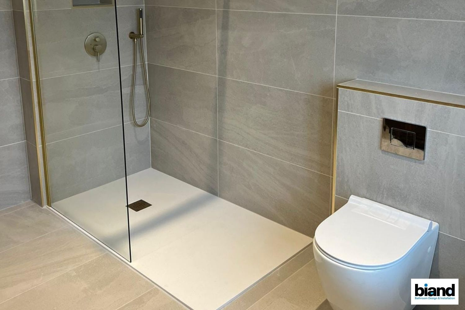 Modern bathroom with a walk-in shower and a white toilet. Gray tile walls and floor, glass shower panel.