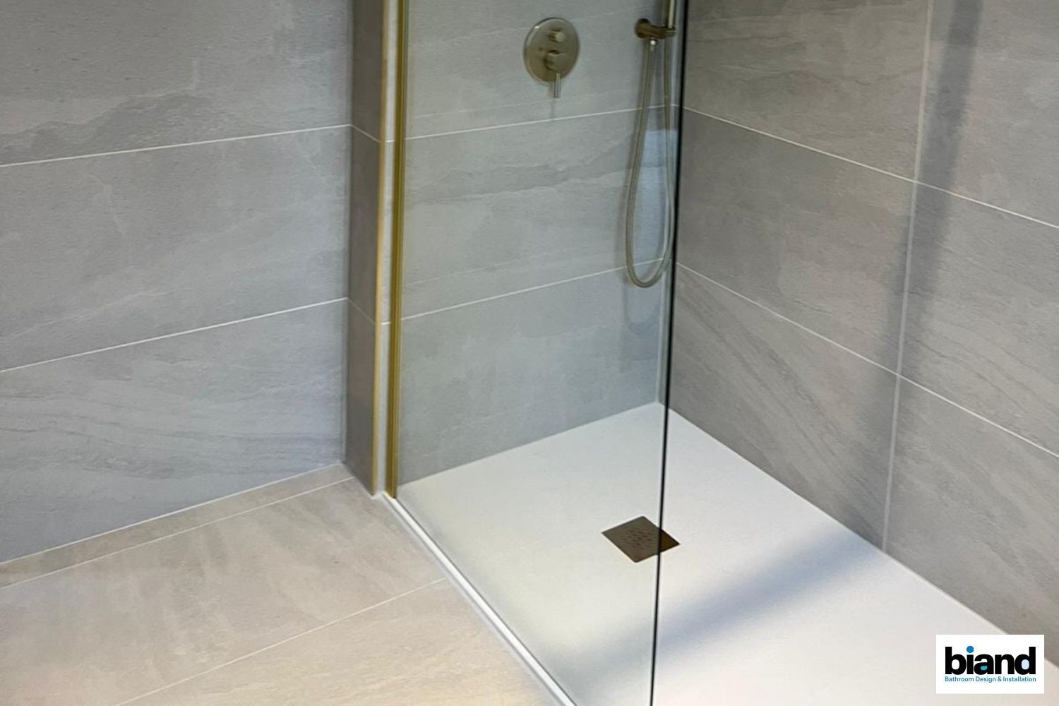 Modern shower with gray tile walls, glass door, and white base.