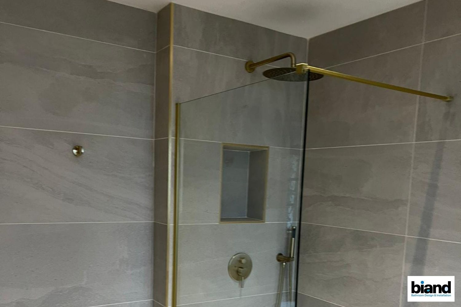 Shower with gray tiles, gold fixtures, and a glass enclosure.